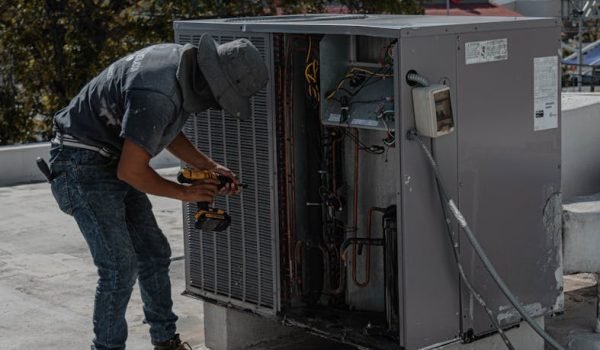 pexels-photo-5463587-5463587-1 A worker in a bucket hat repairs an outdoor air conditioning unit on a rooftop.